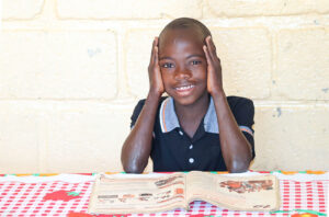 Niño de 7 años sonriendo en un centro educativo de NPH Haití, en un entorno seguro y cuidado.